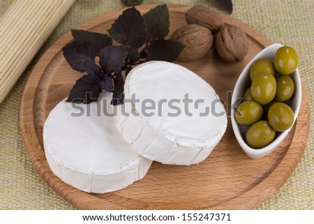 Cheese platter with nuts and grapes, olives and herbs on a wooden plate