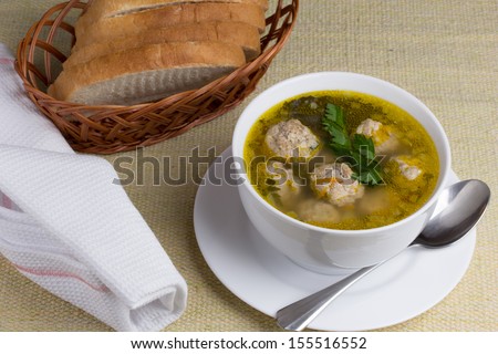 A plate of vegetable soup with meatballs on a white plate with bread