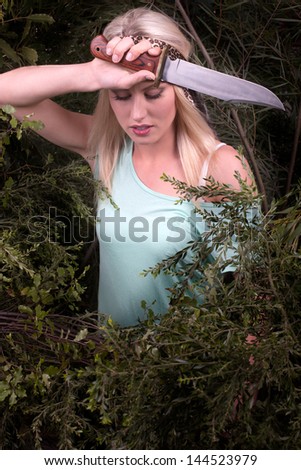 A woman rests from cutting her way through thick bushes with a large knife. The bush is symbolic of life\'s difficulties that seem sometimes to crowd in to our lives and make progress difficult.