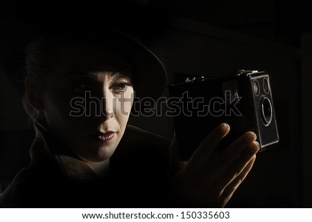 Portrait of a woman holding an old box camera in the style of 1930s film noir.