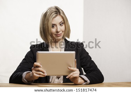 A smart looking young woman looks intently at a digital tablet. She is wearing a business jacket.
