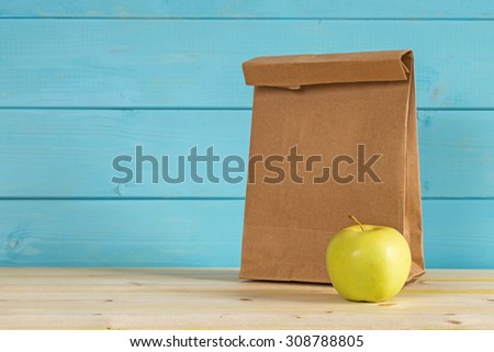 Apple and a paper bag for lunch on a blue rustic wooden background.
