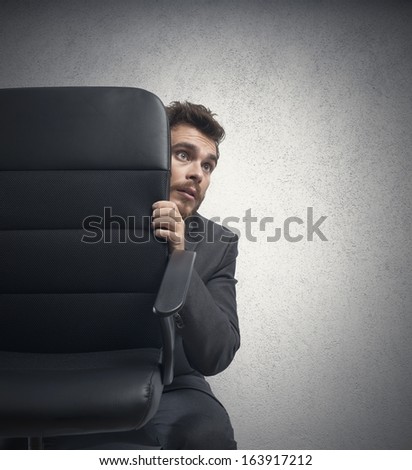 Concept of fear of a businessman behind a chair