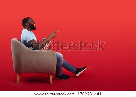 Amused televiewer sitting in the armchair at home while eating popcorns and watching a movie on red background Photo stock © 