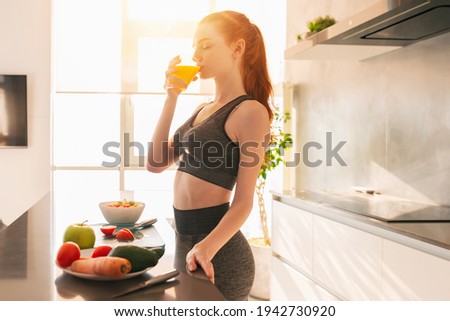 Athletic young red haired woman in the kitchen drinks a glass of fruit centrifuged juice Imagine de stoc © 