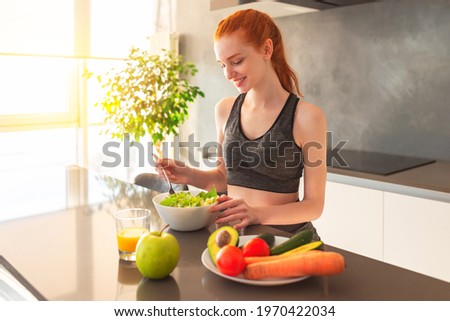 Athletic young red haired woman in the home kitchen eating a healthy salad Imagine de stoc © 
