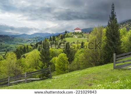 Landscape of pine forests in the mountains with a home away under a gloomy sky.