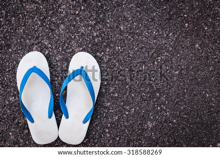 Pair of white plastic flip flop shoe on black asphalt road