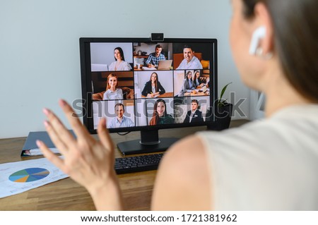 Morning meeting online. A young woman is using app on pc for connection with colleagues, employees. Video call with many people together. Back view
