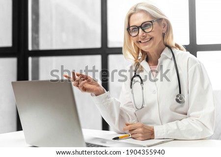 Smiling female doctor pediatric, physical, therapist wearing a white medical gown with a stethoscope on the shoulders using a laptop for video conferencing with a patient. Telemedicine concept Photo stock © 