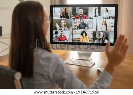Morning meeting online. A young woman is using app on pc for connection with colleagues, employees. Video call with many people together. Back view