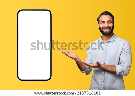 Excited handsome hispanic bearded man points palms at huge smartphone with empty blank screen isolated on yellow, happy indian guy presenting mobile app, showing best deal, copy space, template Foto stock © 