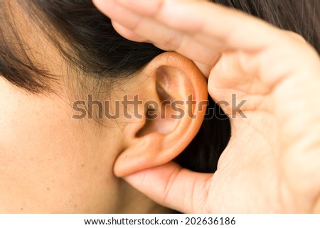 Extreme close-up of a young woman with hands cupped on ear and trying to listen