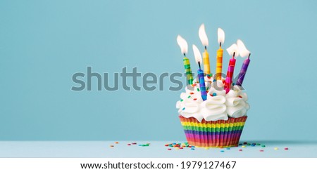 Birthday cupcake with lots of colorful birthday candles against a blue background with copy space to side