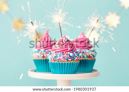 Three birthday cupcakes with pink frosting and party sparklers