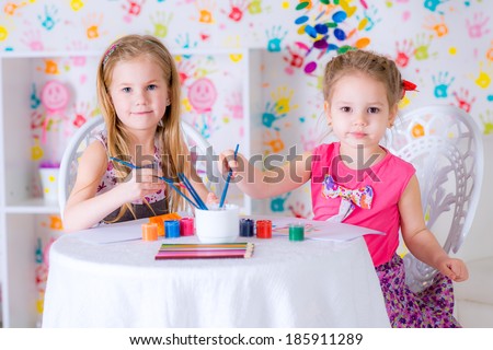two happy girls draw  paints at home in bright living room looking at camera