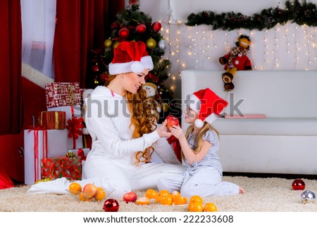 Mom and daughter at home in santa hat near Christmas tree with apples and tangerines