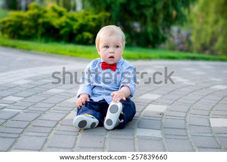 little baby in the park in jeans and a blue shirt in a red bow tie sitting on the track