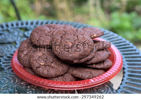 pile of chocolate cookies on red plastic plate on iron table in garden