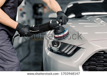 Car detailing and polishing concept. Hands of professional car service male worker, with orbital polisher, polishing white luxury car hood in auto repair shop