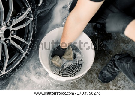 Car wash and detailing concept. Top view of washing tools in car wash service, white bucket with soap cleaning solution, special grille. Hand of male worker holding sponge for cleaning car rims Stock fotó © 