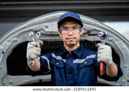 Close-up, a confident Asian auto mechanic holds a wrench and inspects a maintenance vehicle as per customer's claim order in a garage. Auto repair service. Engine maintenance and repair concept. Stok fotoğraf © 