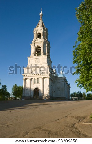 high bell tower of white church on evening light