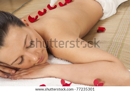 woman in spa lying with red rose petals on her\'s back