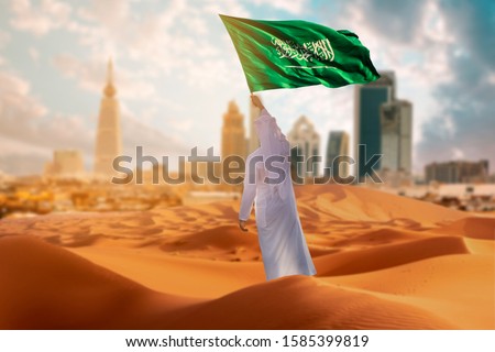 Saudi young Arab man holding Saudi Arabia  flag, celebrating the national day
