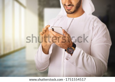 Close up shot of Arab Middle East man using smart mobile phone device browsing the internet or reading emails wearing Kandura and Ghutra