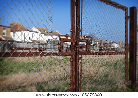 Social housing with fence and wasteland. Old metal gate to field with houses in background