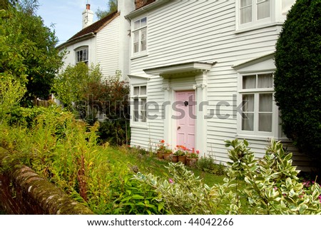 wooden cottage in great britain or england. small wood house with garden in front and pink door.cosy historic  homes in village location