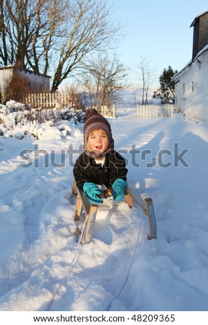 child on sledge or sleigh in winter snow. kid playing on leisure equipment having fun