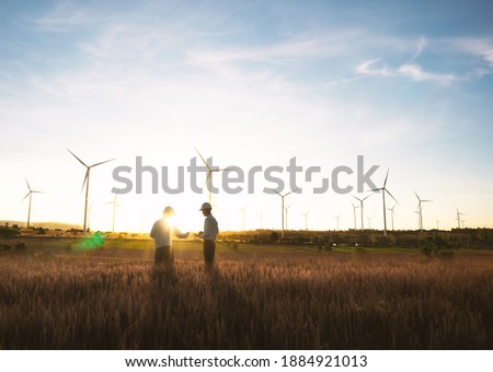 Investors and technician who are out of focus in the foreground are standing in talks about wind turbine power generation, Wind turbine farm is an alternative electricity source for business.