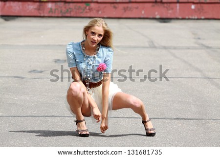 Full length portrait of young blonde woman sitting on asphalt