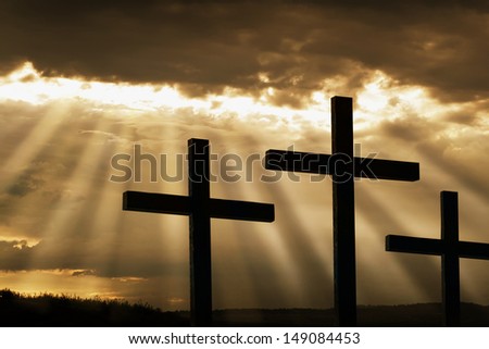 Dramatic sky silhouettes three wooden crosses with shafts of sunlight breaking through the clouds. A dramatic and inspiring religious photographic illustration for Easter or Christian beliefs