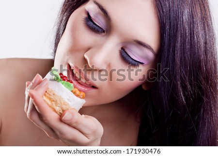 Portrait of young beautiful woman eating cake on a white background. Enjoy the food. Brunette with fashion pink makeup with false eyelashes.