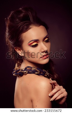 Portrait of young beautiful brown-eyes woman with fashion hairstyle and orange yellow makeup. Fashion model shooting. Gold blue jewelry.