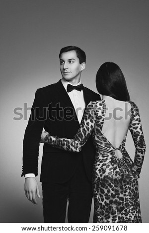 Young couple of fashion models dressed in elegant classic evening clothes: suit, bow tie, animal-print leopard open back dress on white background. luxury. Italian style. Sexuality.  Sensuality.