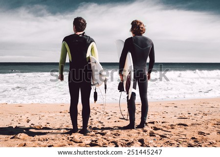Two surfers are looking at the ocean and waiting for a big wave