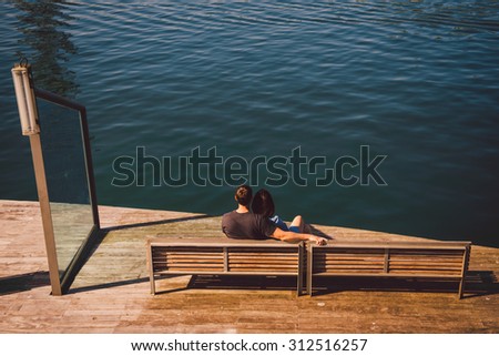 Couple in love is sitting on the bench hugging and looking at the ocean panorama