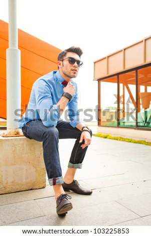 attractive young male model posing outdoors in blue shirt and sunglasses