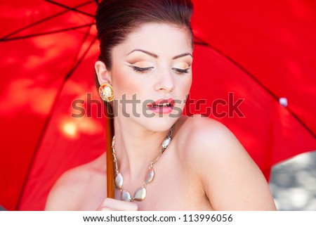 beautiful woman with perfect skin wearing professional make-up holding a red umbrella