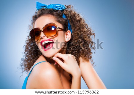 cute pin up girl with perfect teeth smiling, curly hair and sunglasses on blue background