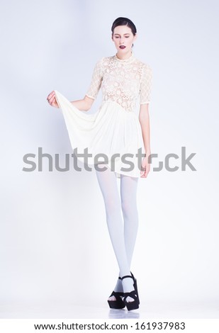 beautiful woman with long legs in white dress and high-heels posing in the studio