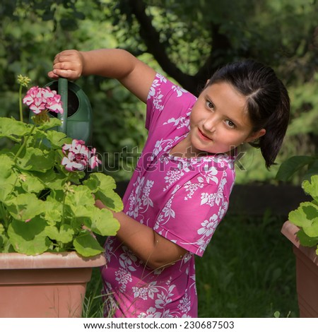 Happy little girl watering flowers in a pot, gardening.