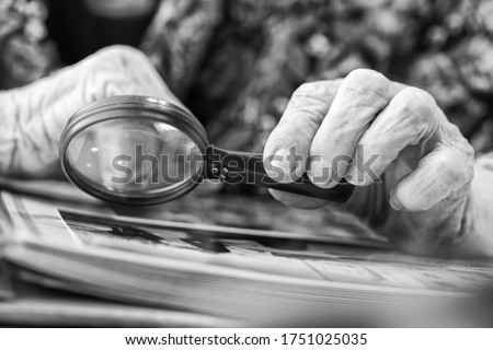 An old grandmother examines a book at the table with a magnifying glass Foto d'archivio © 