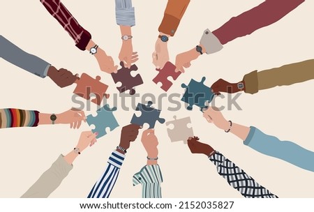 Group of multicultural business people with arms and hands in a circle holding a piece of jigsaw. Co-workers of diverse ethnic groups and cultures. Cooperate - collaborate. Teamwork