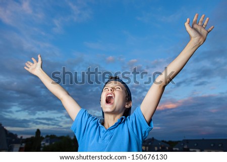 Teenage boy, standing outside, its evening, screaming, celebrating, throwing his arms up in the air