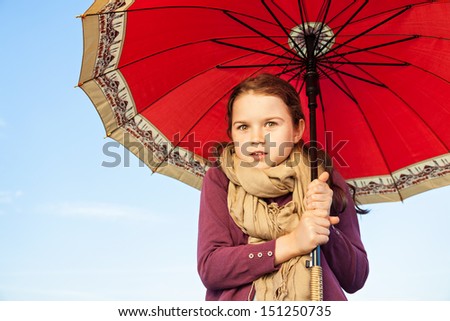 A little girl holding her umbrella  and she is cuddled underneath, she looks like as if she is cold.